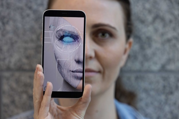 a woman holding a mobile phone in front of her face. On the screen is a digital facial recognition version of her face