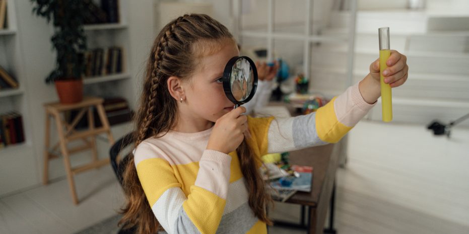 Citizen Science in action: a Child with a magnifying glass inspecting a test tube with a yellow liquid