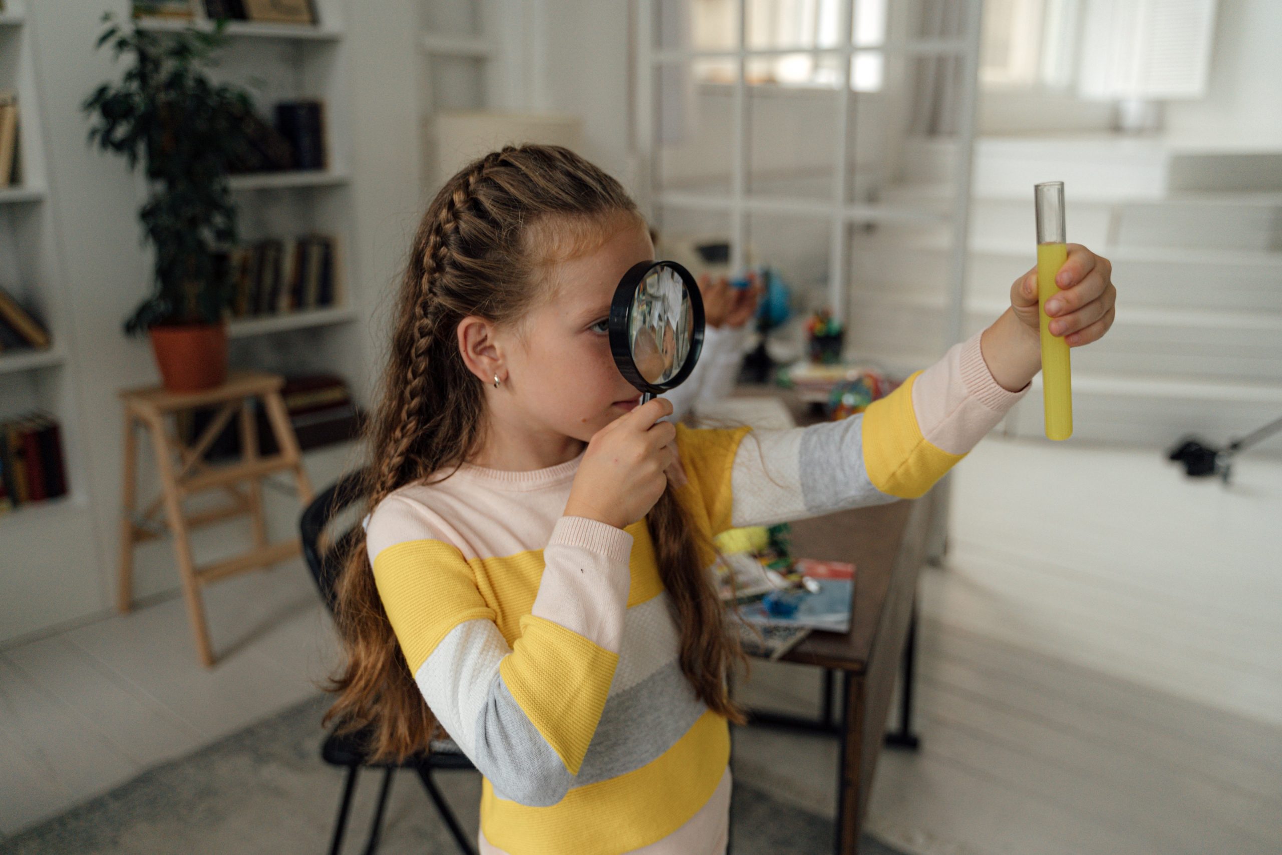 Citizen Science in action: a Child with a magnifying glass inspecting a test tube with a yellow liquid