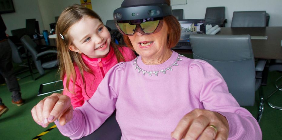 A woman wearing a pink top interacts with a child while wearing a virtual reality headset