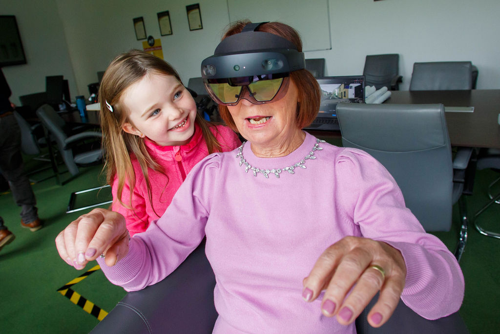 A woman wearing a pink top interacts with a child while wearing a virtual reality headset