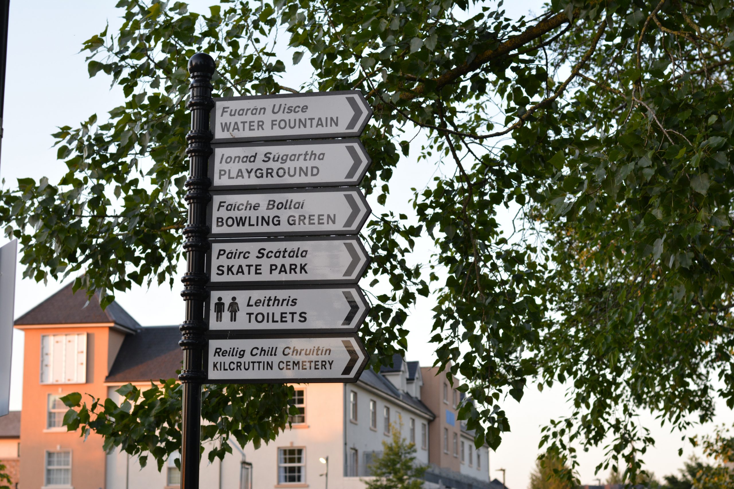 black and white sign post in Tullamore, Co. Offaly. The signpost features 6 individual signs with English-Irish translations for local amenities like skate park (Páirc Scátála), playground (ionad súgartha) and toilets (leithris)
