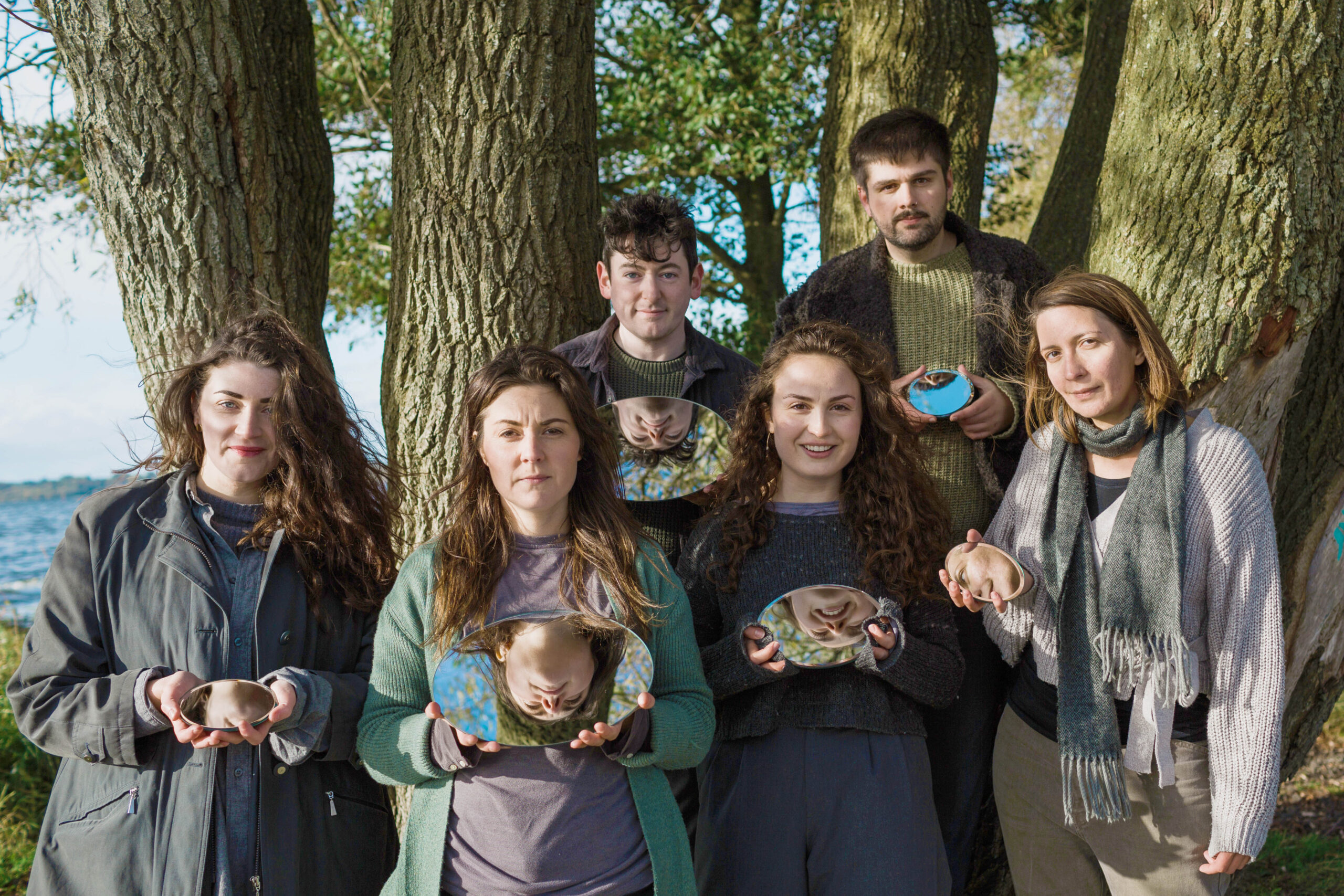 A promo pic for HIVE choir. Choir members are posing in a forest, each holding a mirror reflecting their face.