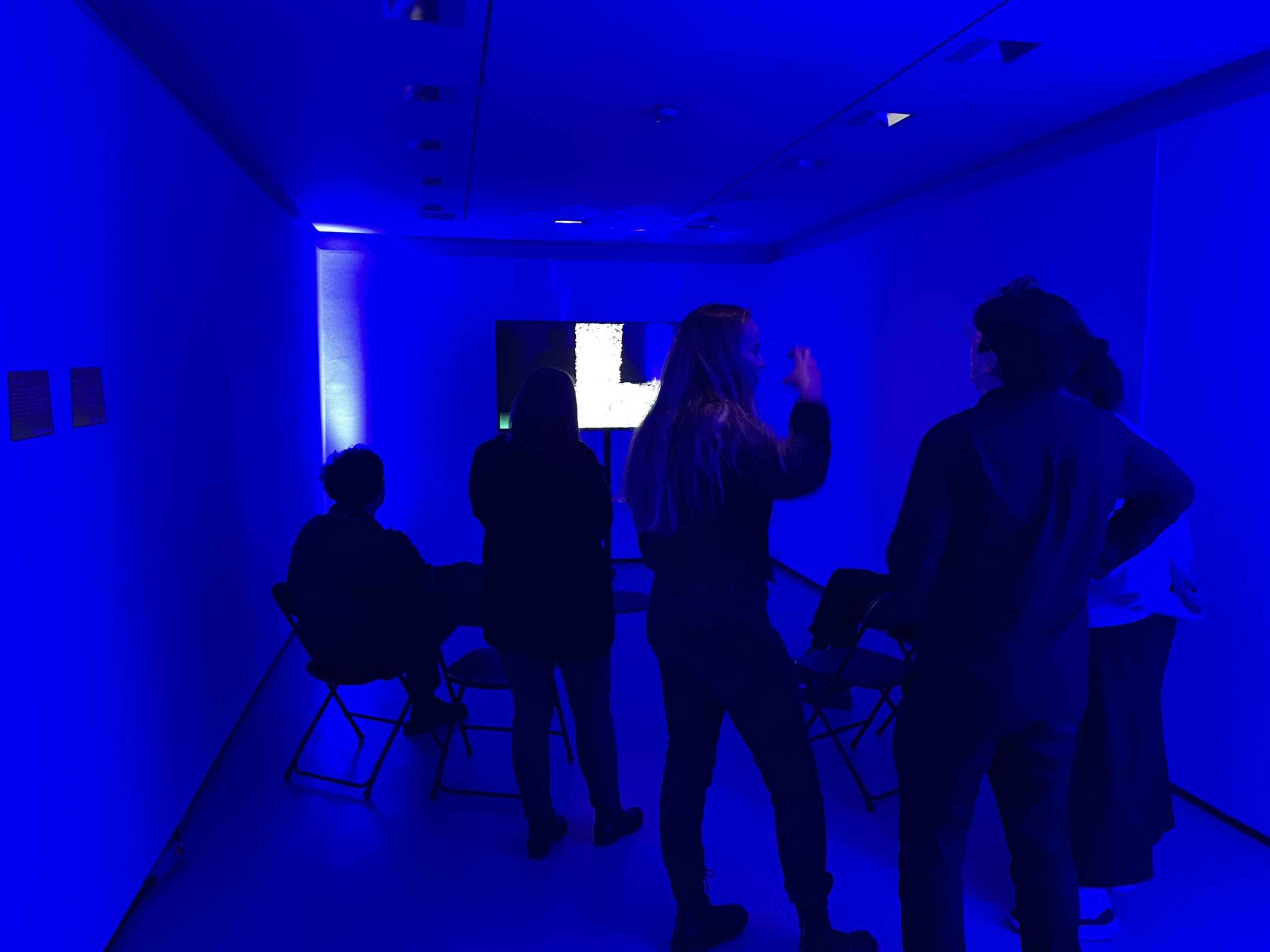 People chatting in a blue room with some video artwork on a screen in the background