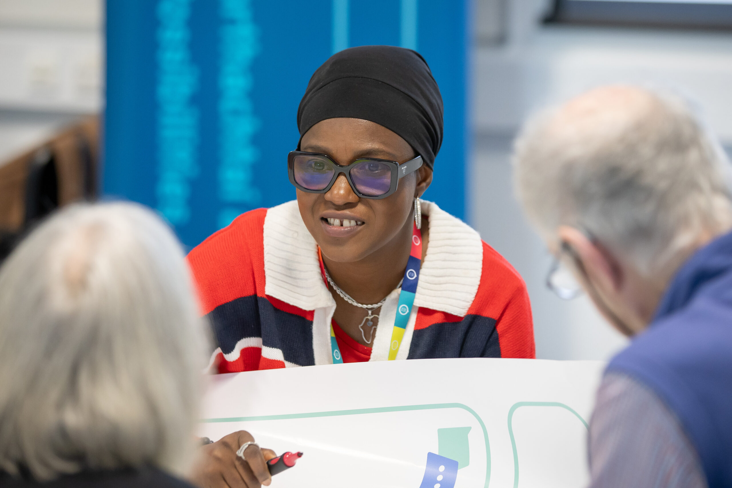 A lady with dark glasses and headscarf (ADAPT researcher Fatima Badmos) smiles as she chats to a man and a woman at a #DiscussAI think-in